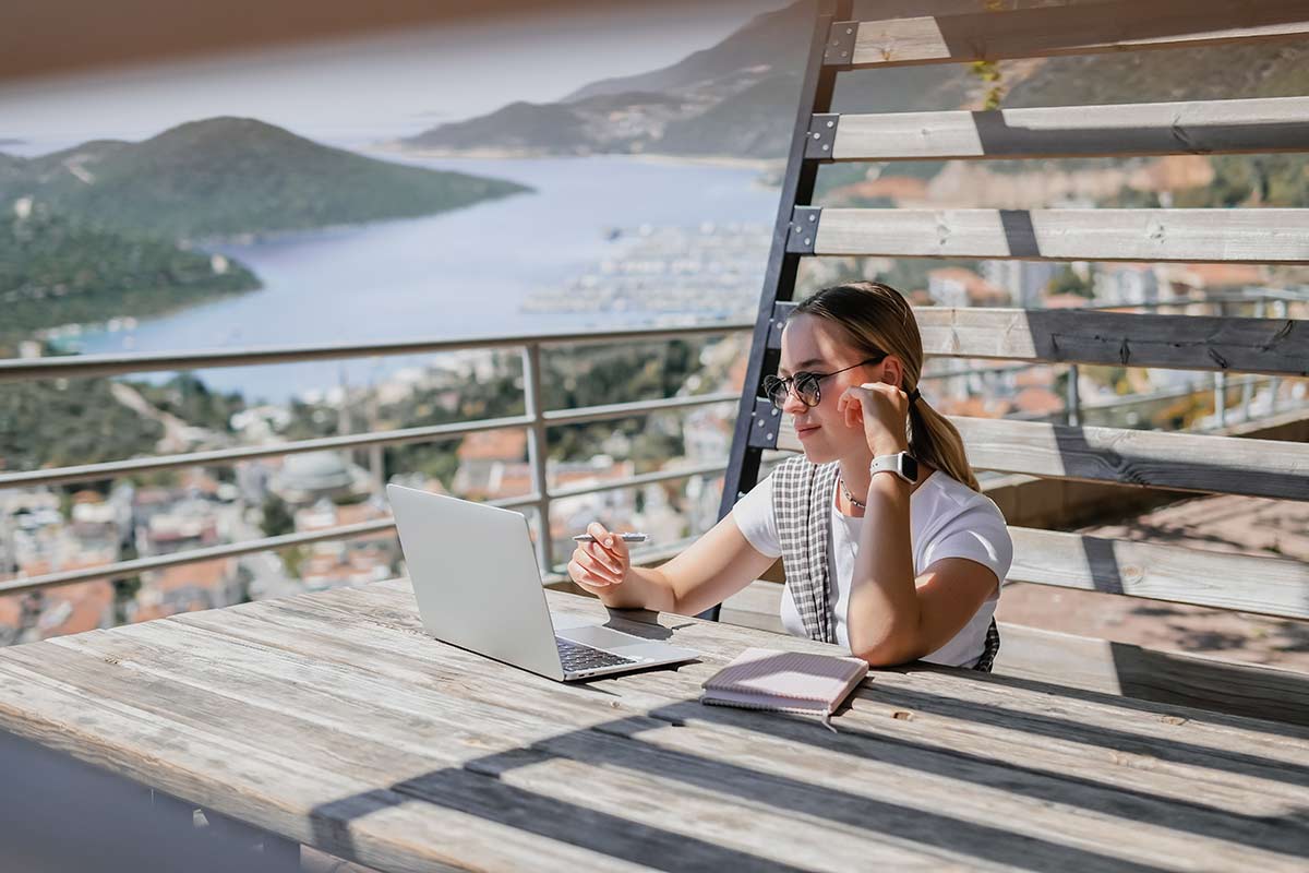 Mujer trabajando con el ordenador en una terraza con vistas al mar